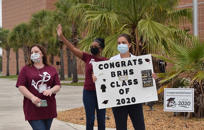 School nurse Dayna Grella, receptionist Avis Boldin and school counselor Kirsten Lawlor cheer and wave to seniors as they pick up their caps and gowns.