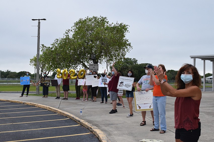 Families cheer with signs congratulating their seniors.