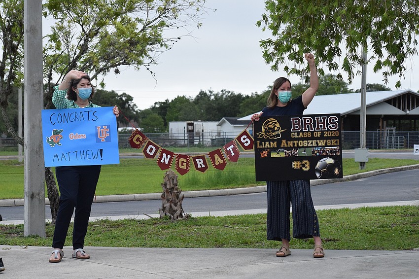 Sara King and Holly Antoszewski wave to their sons Matthew King and Liam Antoszewski as they drive by after picking up their caps and gowns. 
