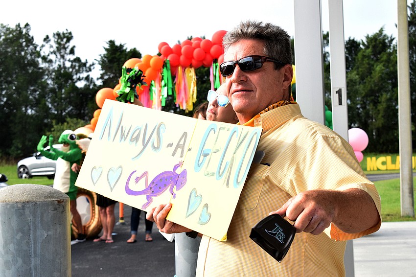 Roy London, an art teacher at Robert E. Willis Elementary School, shows his hand-drawn sign to students while ringing a cowbell.