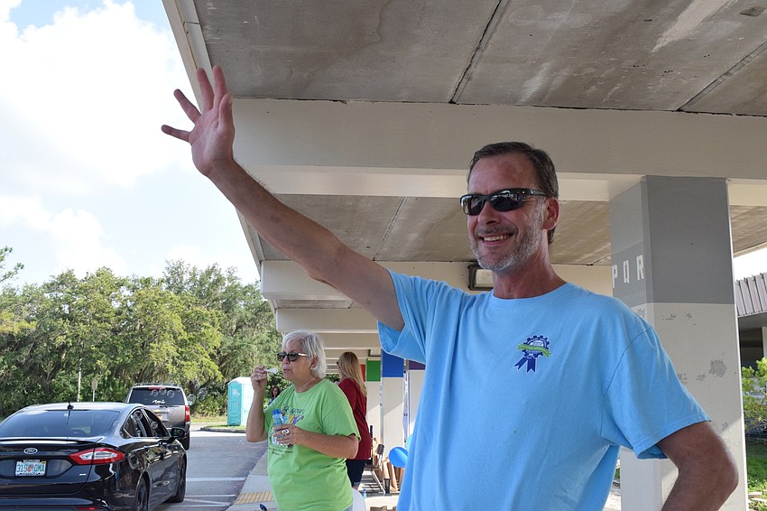 Tom Brugos, a science teacher at Gene Witt Elementary, waves and cheers for fifth graders during a farewell parade.
