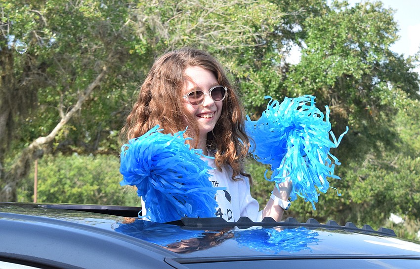 Avery Mankowski, a fifth grader at Gene Witt Elementary, shakes pom poms while standing out of her car's sun roof.