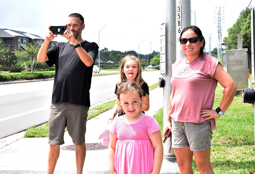 Joel Moore takes video of the Manatee Strong parade while his daughter Kailynn and Abrianna and Abigail Williams watch the buses drive by.