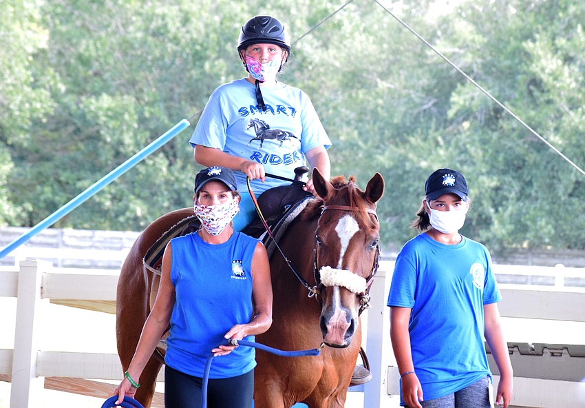 Volunteers Ilee Finochiaro and Ellie Blitz walk alongside camper Gracie Gerling, who is 11, in the arena.