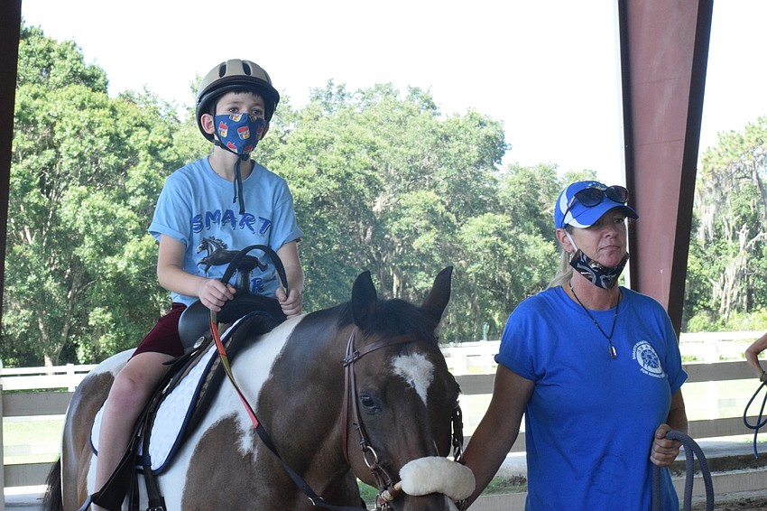 Camper Joseph Woolbert, who is 10, rides Buddy Cassidy while Samantha Toomey, the equine manager, guides them around the arena. Before riding, campers learn about the horses and how to care for them.