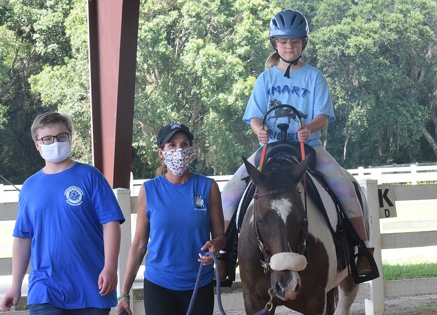 Volunteers Ryan Blitz and Ilee Finochiaro walk alongside camper Angela LeBouf, who is 9. LeBouf was excited to ride Buddy Cassidy.