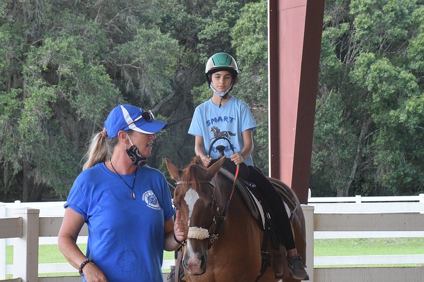 Samantha Toomey, equine manager, directs camper Alexis Mariano, who is 11, where to go in the arena while giving her tips on riding. Mariano has ridden a horse twice before the camp.
