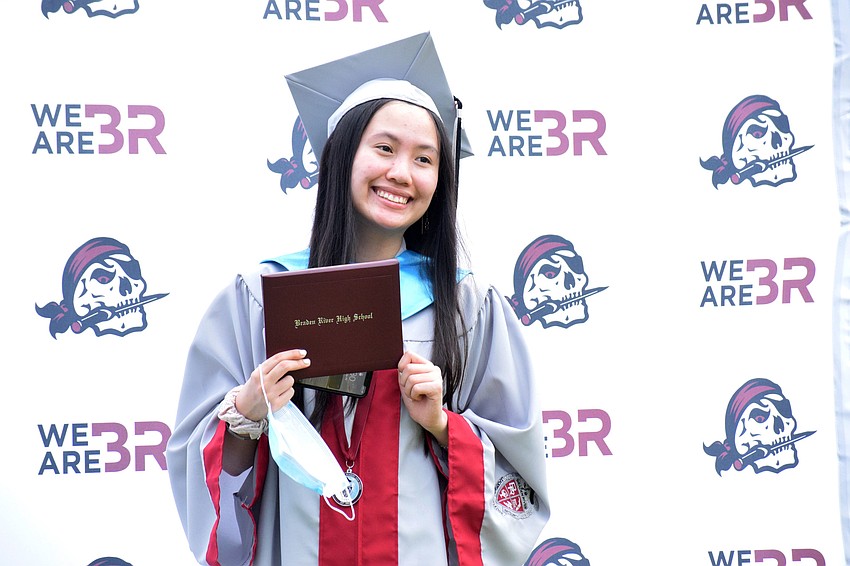 Anna Dong holds onto her mask while having her photo taken with her diploma.