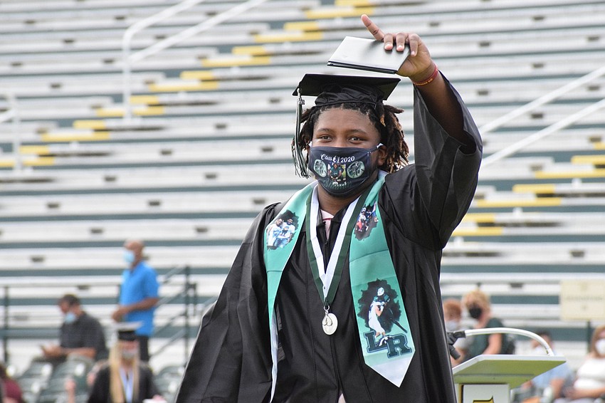 Shamar Beatty points to his family in the stands while walking across the field with his diploma. His sash and mask has photos of memories from his time at Lakewood Ranch High School.