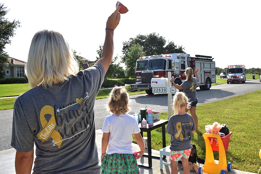 Rachel Wells cheers as her daughters Charlotte and Savannah Wells and Ashlie Fulmer watch firetrucks drive by to celebrate Charlotte Wells' last day of chemotherapy. The emergency service vehicles were a surprise for Charlotte.