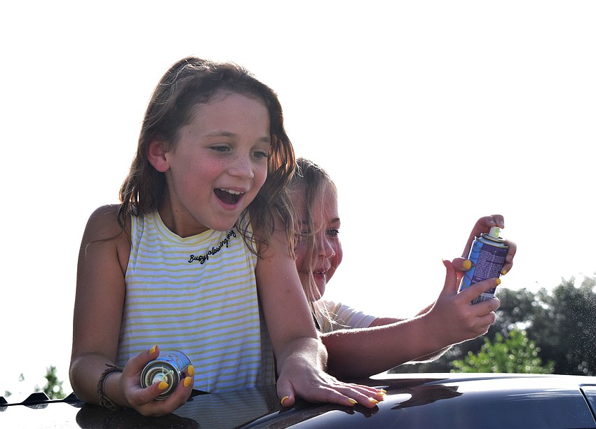 Lillian Chandler and ReAnn Kolbe cheer for Charlotte Wells while standing out of the sun roof of a car.