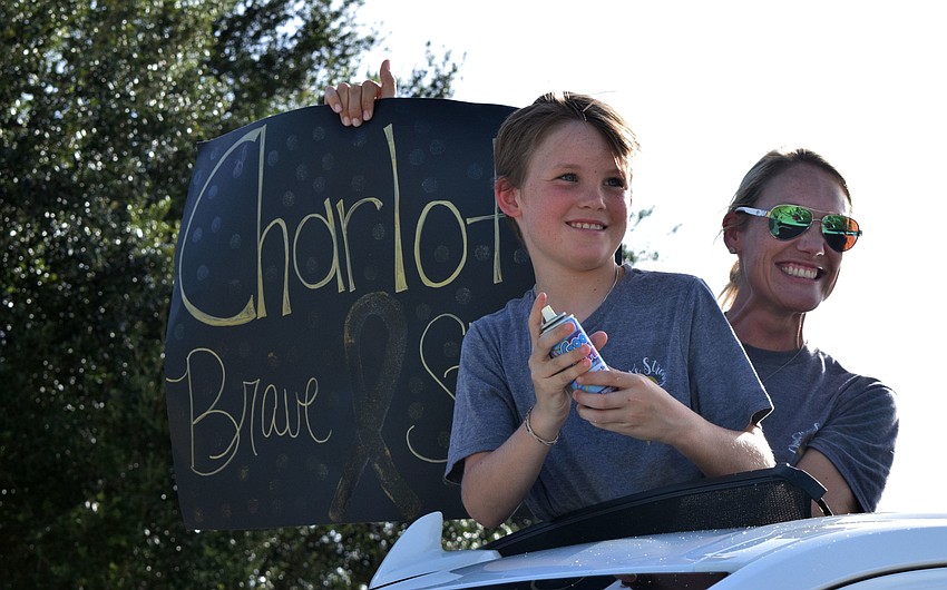 Michael Ryan prepares to spray silly string while his mother, Lindsey, holds up a sign that says 'Charlotte brave and strong.'