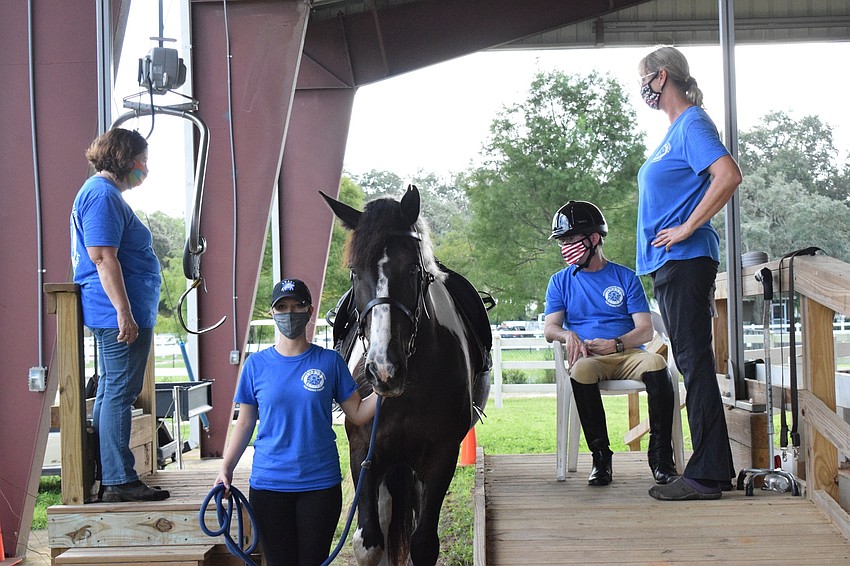 SMART volunteers Corinne Adams and Megan Jones help equine manager Samantha Toomey lift Dan Mohl onto a horse for his riding session.