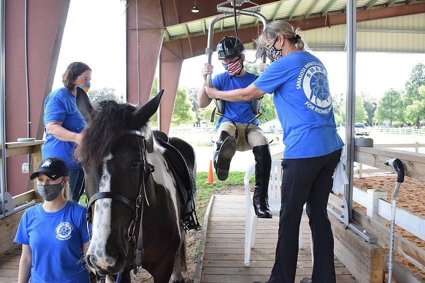 Volunteer Megan Jones holds onto Gallagher the horse while volunteer Corinne Adams and equine manager Samantha Toomey help Dan Mohl get into his saddle.