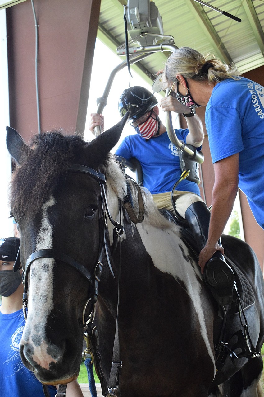 Dan Mohl gets adjusted in the saddle with the help of Samantha Toomey, an equine manager at Sarasota-Manatee Association for Riding Therapy. Mohl must use a lift because he's paralyzed on the left side of his body.
