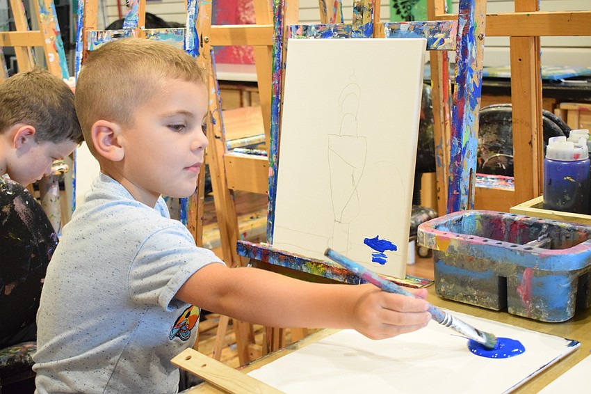 Boden Colon, a kindergartner at Robert E. Willis Elementary School, dips his brush into blue paint so he can paint the table on the canvas.