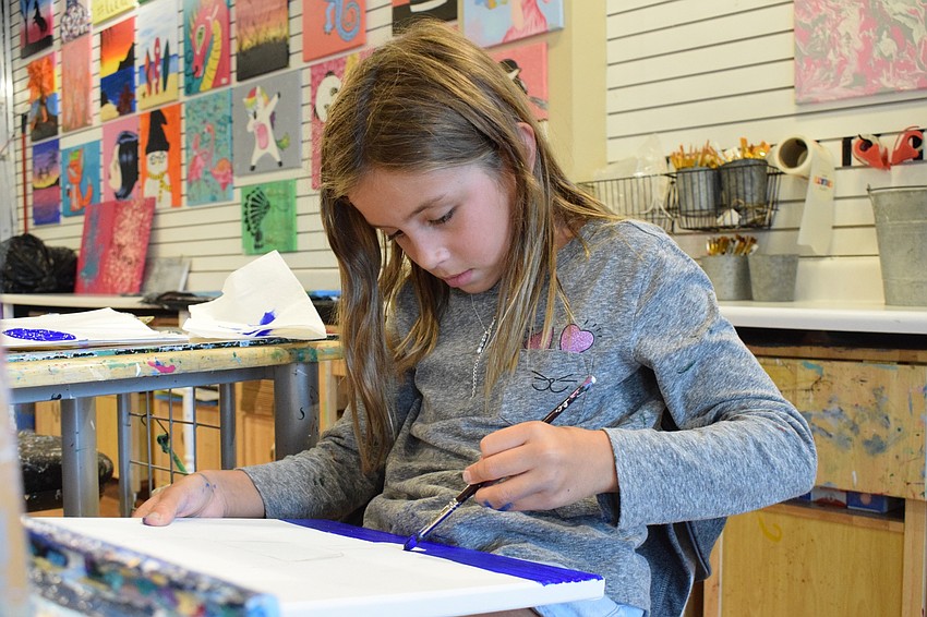 Charley Birdsall, a third grader at Robert E. Willis Elementary School, meticulously paints a canvas. Birdsall is painting a Cookie Monster ice cream scoop with dark pink drizzle.