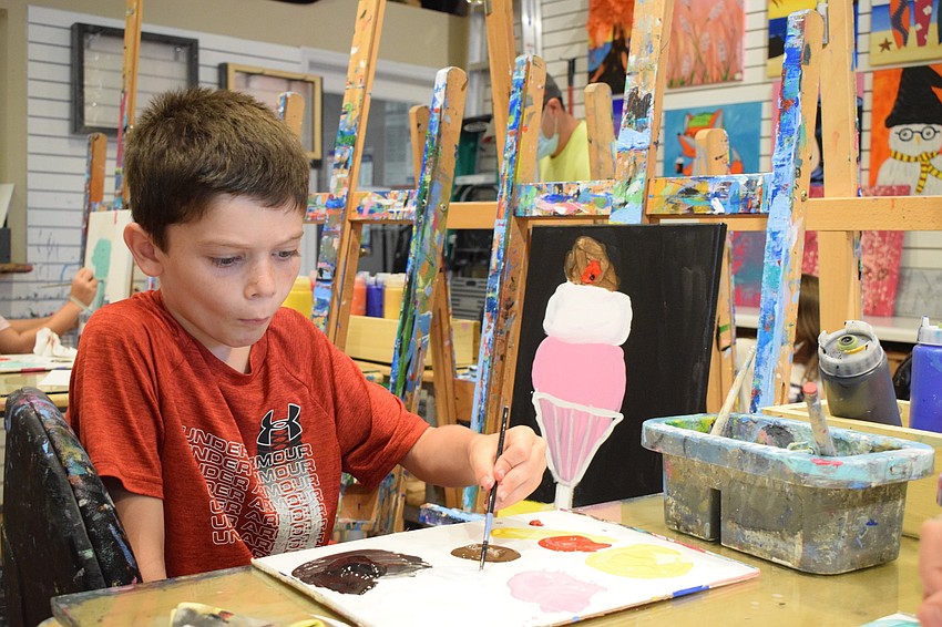 Mark Kloss, a first grader at Providence Community School, dips his brush into paint before continuing his ice cream sundae painting.