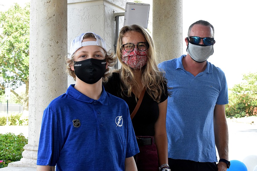 Thirteen-year-old Weston Hermann waits with his sister Makenna Hermann and father, Jared Hermann, in front of the clubhouse for the next car to come through the drive thru fundraiser.