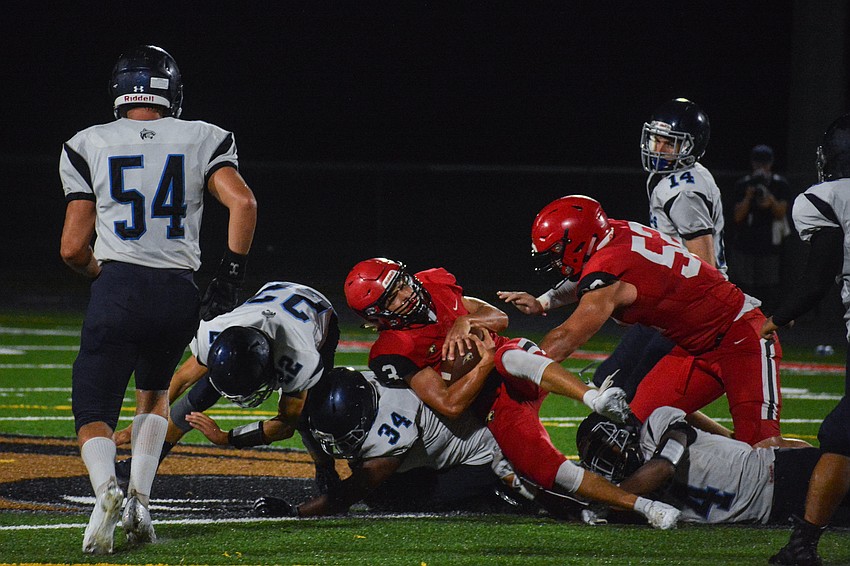 Cardinal Mooney quarterback Tayven Clark takes a hard hit from North Port defenders and holds onto the ball.