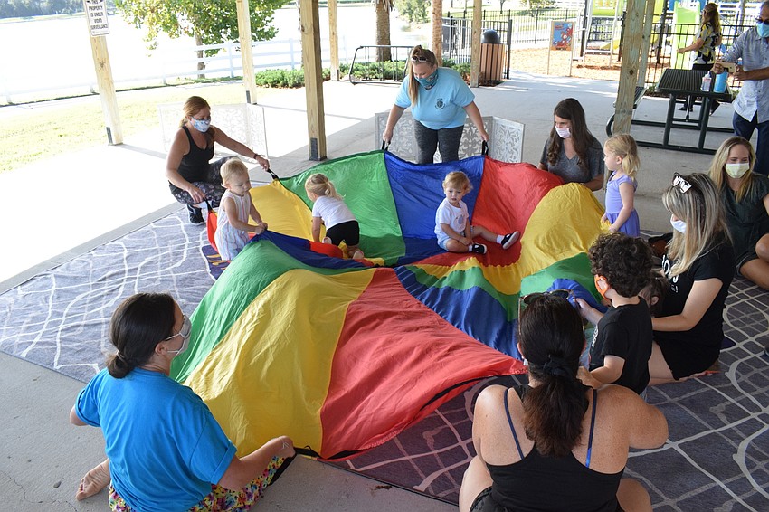 The moms move the parachute around and sing while the children play on top.