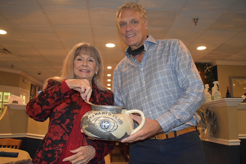 Lynn Larson drops happy dollars into the Kiwanis pot held by Chris Sachs.