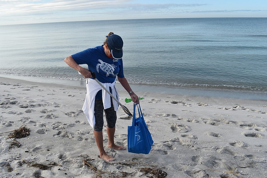 Nancy Rozance uses a trash grabber to pick up tiny bits.