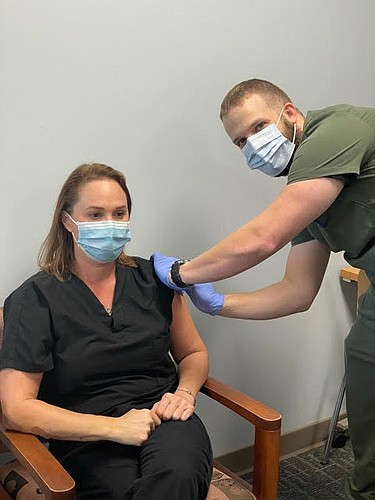 Vanessa Spingola, the emergency department clinical leader for Lakewood Ranch Medical Center receives the hospital&#39;s first Moderna COVID-19 vaccination from  Derek Whitecotton, a hospital pharmacist.