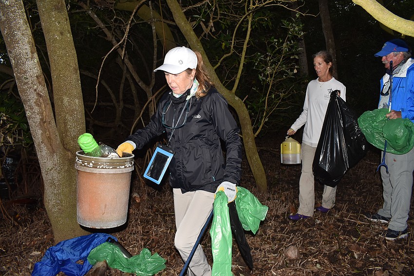 Lyn Haycock carries a bucket of trash to a waiting boat.