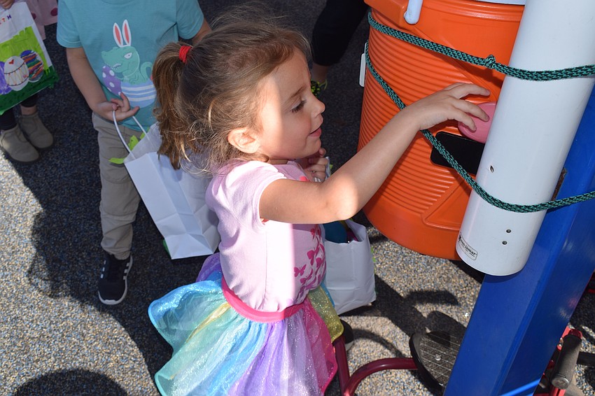 Brielle Pauling, who is 4 years old, finds an egg hiding by the water container attached to the playground equipment.