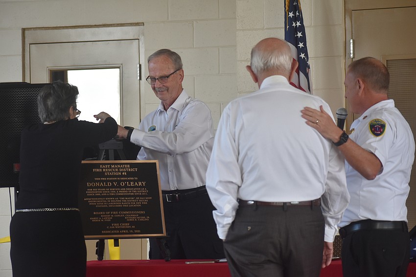 Audrey O'Leary and East Manatee Fire Rescue District Commissioner Bob Conley unveil a plaque commemorating East Manatee Fire Station 8 to former fire commissioner Don O'Leary as O'Leary and Fire Chief Lee Whitehurst look on.
