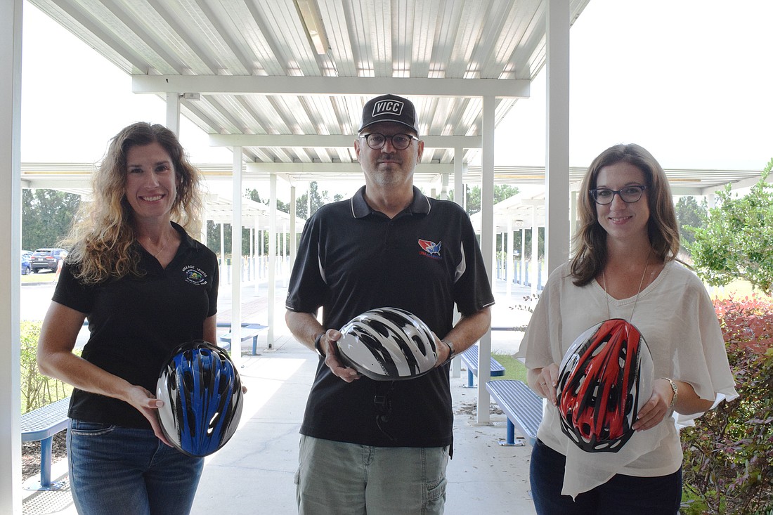 Dawn Zielinski, president of the Village Idiots Cycling Club, and Tom Williams, outreach director for the club, donates bike helmets to Megan Podolan, a fifth grade teacher at Willis Elementary School, to give to students.