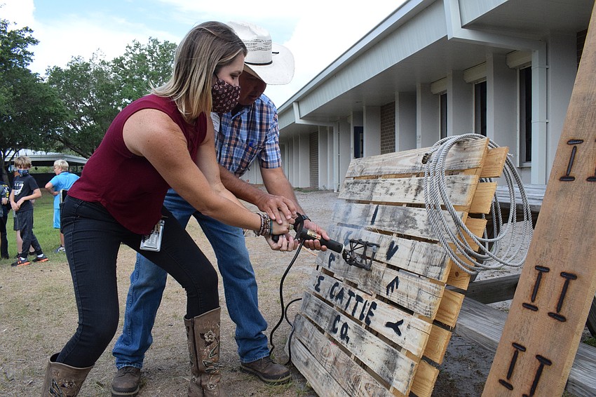 Ellie Dauphas, a fourth grade teacher, and Brian Broxson with Blackbeard's Ranch brand a sign that will go in Dauphas' classroom. The MacIvey Cow Company sign is from the book 