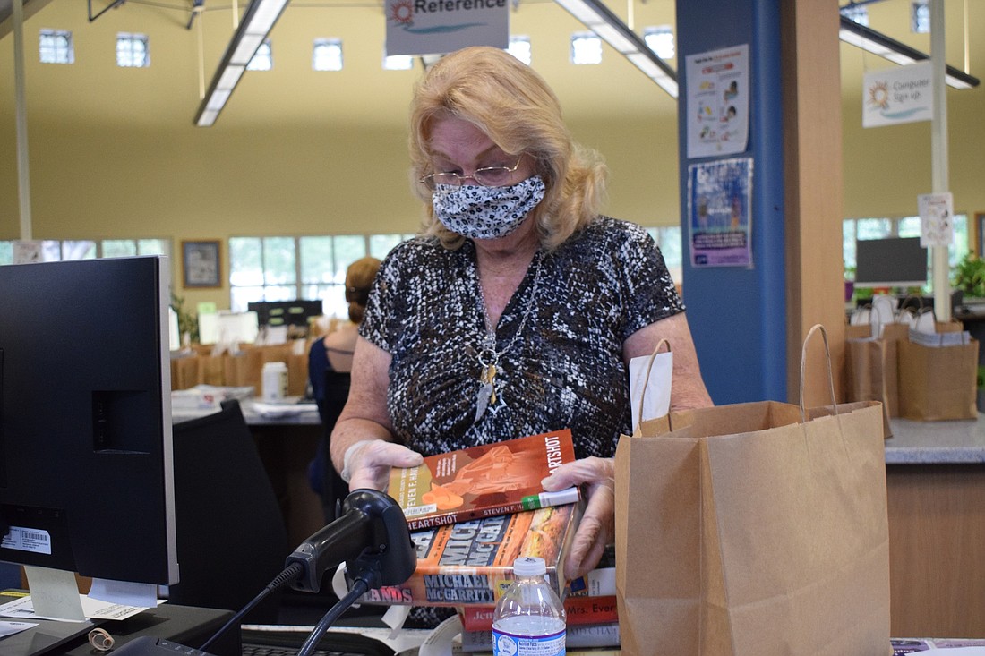 Cathy Habora, a library assistant, checks out books before placing them in a brown paper bag and putting them on the table outside for someone to pick up. Curbside services will be available June 8 through July 24.