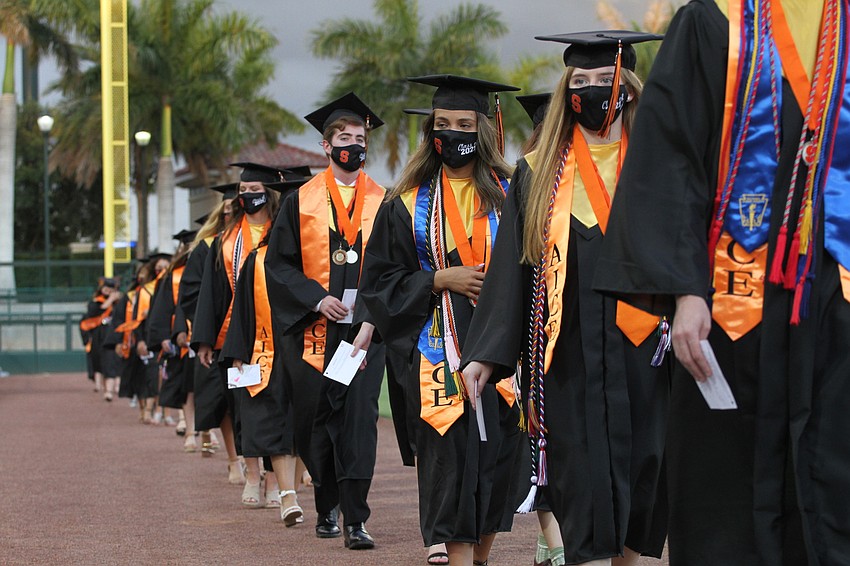 Graduates walk in two lines to their seats.