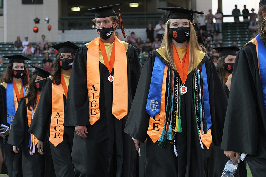 Graduates walk in two lines to their seats.