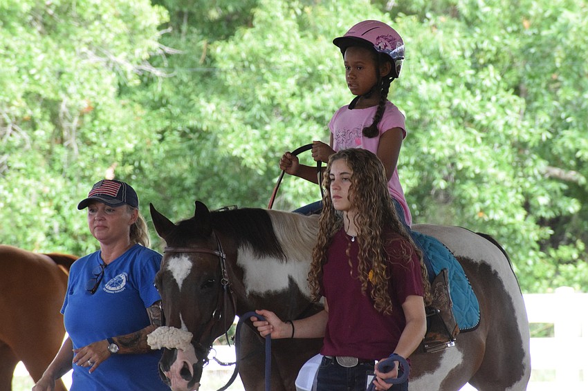 Sabrina Bosarge, a PATH instructor in training, Taelyn Chapman, a camper, and volunteer Natalie Debaets make their way around the arena.