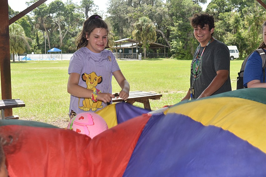 Sarasota's Madison Kukoda, 10, and camp counselor Riley DiCosola play a game in which people stand in a circle and move a sheet up and down in order to bounce a ball in the air and prevent it from touching the ground.