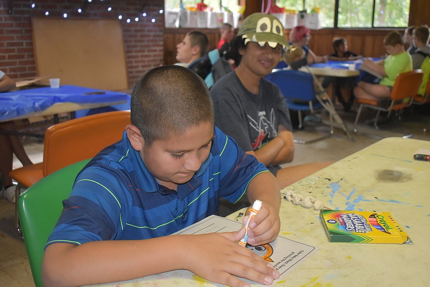 Fort Myers' Isaac Ortiz, 9, colors next to counselor Cynthia Lukose during arts and crafts time. In addition to arts and crafts, Ortiz said his favorite part of the camp was horseback riding, even though it was bumpy.