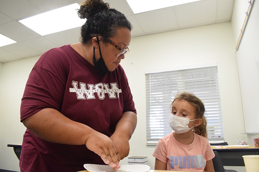 Melissa Mayoral, a Camp Banyan leader, shows Abigail Lakatos how to smash her clay onto the plastic plate so Lakatos can later use it to attach her coral.