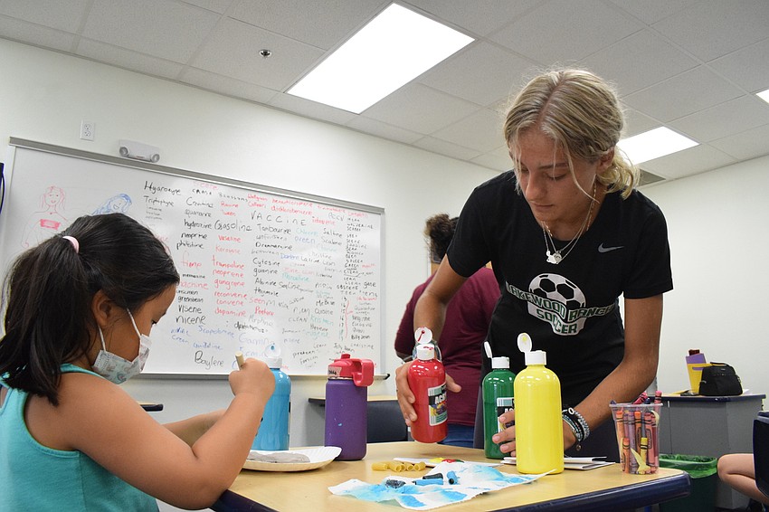 Grace Dokko continues to paint her noodles while Makena Murack, a camp counselor, provides her more colors of paint.