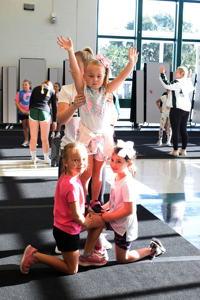 Elin Anthony, who is 7, and Finley Warner, who is 6, hold up Blaire Wilson, who is 6, while practicing stunts.