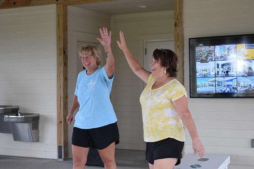 Kelly Harmon and Carolyn Ray high-five after Ray tosses her bag into the hole of the cornhole board scoring three points.