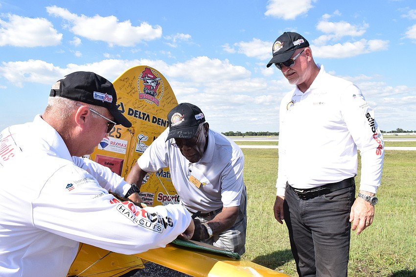John Swan with Dream Flights, holds onto a poster that Melvin Pettis, a Cypress Springs Gracious Retirement Living resident and Navy veteran, signs while Darryl Fisher, the president and founder of Dream Flights, watches.