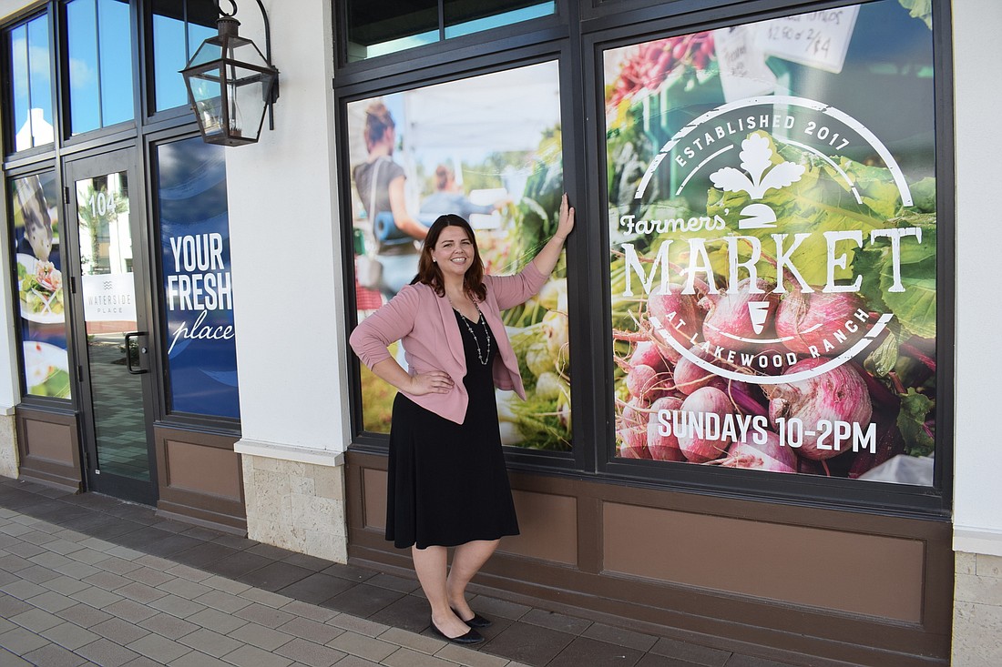 Monaca Onstad stands at Waterside Place in front of a window promoting the farmers market.