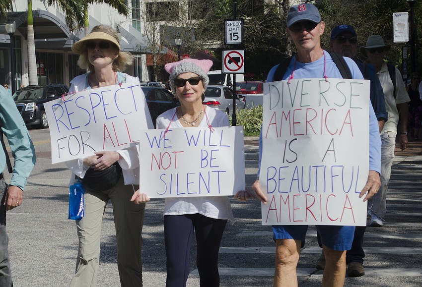 Lori Gelbort, Helane Abramowitz and Bruce Abramowitz wear their signs while walking to Bayfront Park for the Women’s Solidarity March.