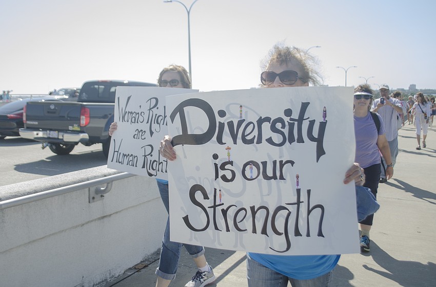 Carol Stone and Karen Kates hold signs as they march across the Ringling Bridge.