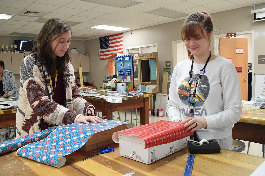 Fiorella Recchioni and Sarah Douglas, seniors at Braden River High School, start wrapping shoe boxes that will be put in classrooms as donation boxes.
