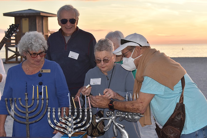 Phyllis Dreyfus, Irv Ross, Sally Steel and Jay Steele work to light the menorah in the evening breeze.