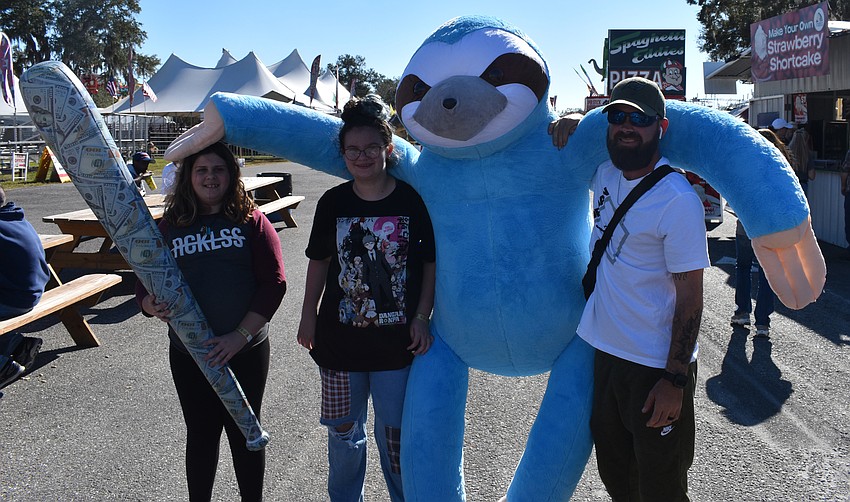 Allison Bizata, Kailee Hooey and Al Barrett, all of Bradenton, show off their giant prizes — including a huge blue stuffed sloth — in the midway.